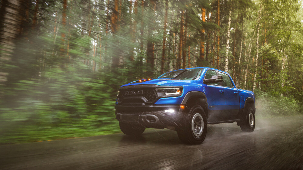 Blue lifted Ram truck driving down a dirt road in a forest. 